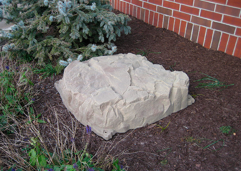 A gray decorative rock laying in a garden bed near the exterior wall of a house.